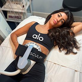 Female patient chilling at Blue Water Spa while being treated with Emsculpt on her abdomen.