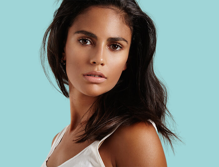 A confident woman showing her flawless complexion in a blue background. [1d9d83]